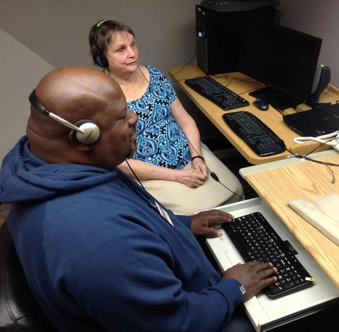 Instructor, Ann, with student wearing headphones sitting at computer