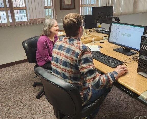 Instructor, Linda, sits next to student who is a veteran. Both face the computer.