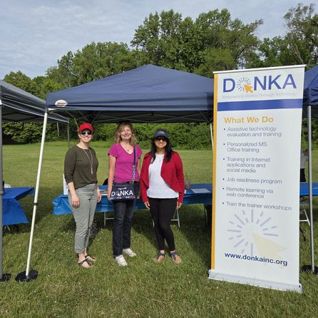 Abby, Rhonda and Anum smiling next to Donka sign in front of table