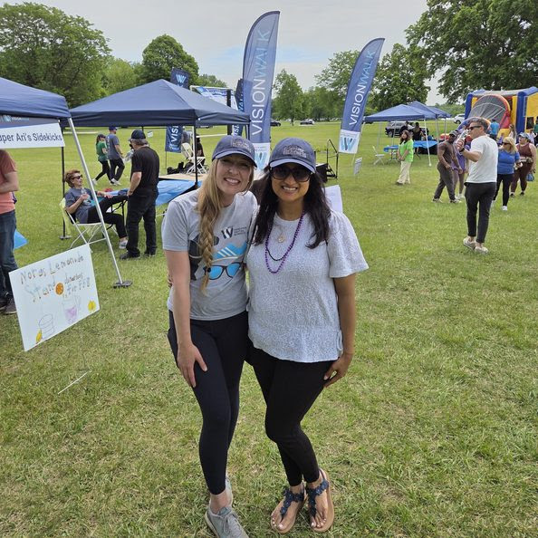 Jenni and Anam smiling in front of tents at Vision Walk